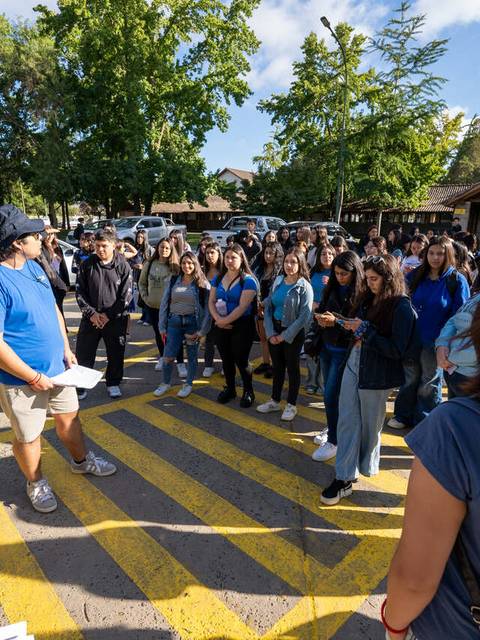 Un grupo de personas se reúne en una calle con rayas amarillas, mientras un hombre habla frente a ellos.