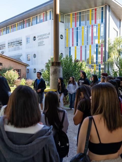 Grupo de estudiantes en un campus universitario frente a un edificio moderno.