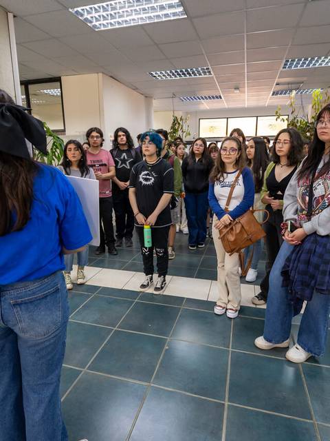 Un grupo de estudiantes escucha atentamente a una persona que les habla en un espacio interior.
