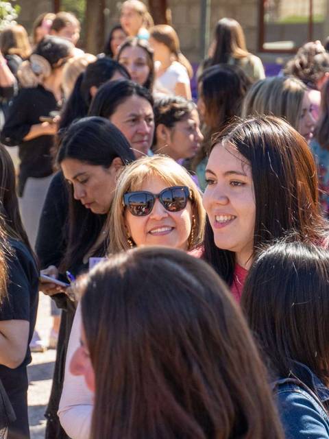 Un grupo grande de mujeres sonriendo y conversando en un evento al aire libre.