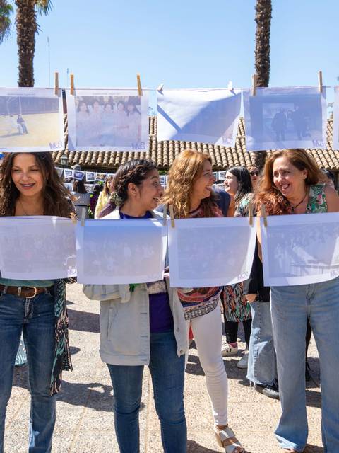 Un grupo de mujeres participa en un evento al aire libre, exhibiendo fotografías colgadas en cuerdas durante una jornada de celebración.