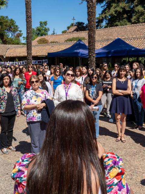 Un grupo numeroso de mujeres escucha atentamente a una oradora en un evento al aire libre.