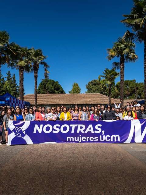 Un grupo de mujeres se reúne al aire libre detrás de un banner que dice 'NOSOTRAS, mujeres UCM'.