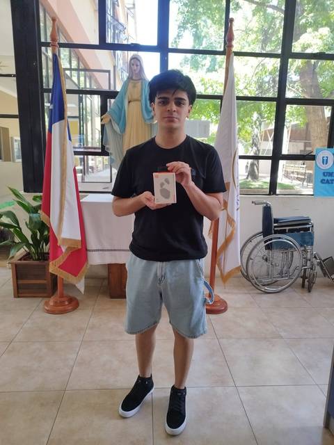 Un joven sosteniendo una caja en un entorno interior con banderas y una figura religiosa detrás.