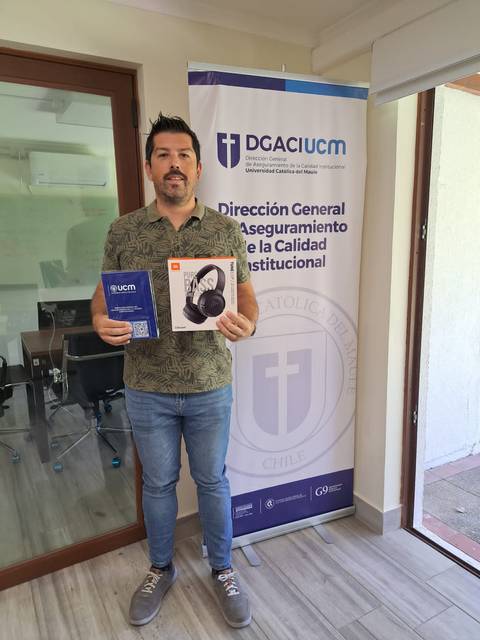 Un hombre sostiene un paquete de auriculares y un documento frente a un cartel institucional.