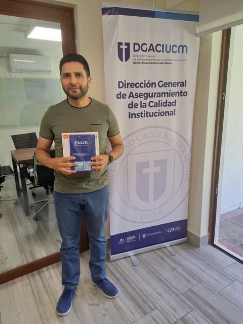 Un hombre sostiene un libro mientras posa frente a un cartel de la Dirección General de Aseguramiento de la Calidad Institucional.