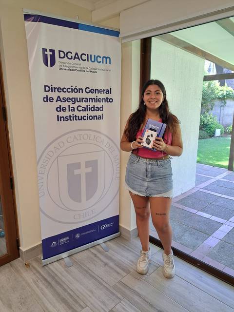 Una persona sostiene un objeto frente a un banner institucional en un ambiente luminoso.