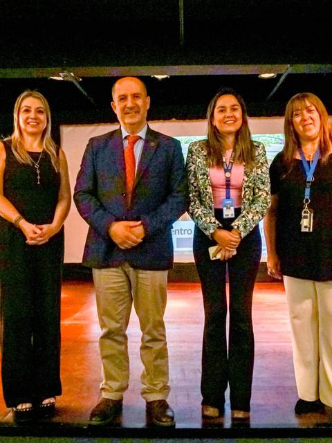 Un grupo de seis personas posan frente a un fondo de presentación en un evento formal.