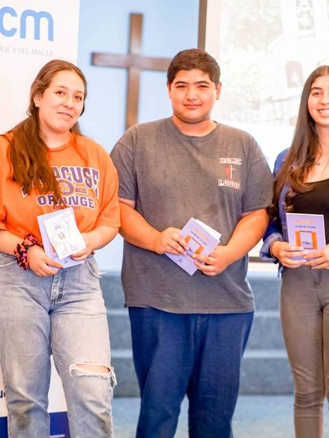 Tres estudiantes posan juntos sosteniendo libros en un evento en la universidad.