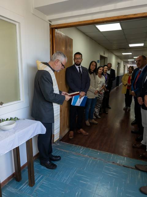 Un grupo de personas asiste a una ceremonia en un pasillo con una mesa decorada en un lado.