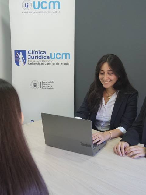 Dos mujeres jóvenes conversan en un ambiente profesional frente a una computadora portátil.