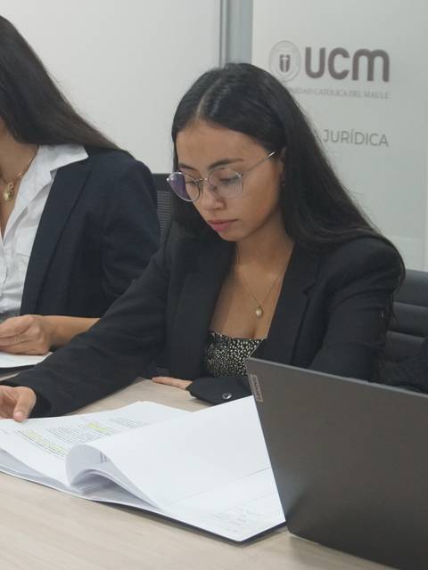 Tres mujeres trabajando juntas en una mesa de oficina con documentos y computadoras portátiles.