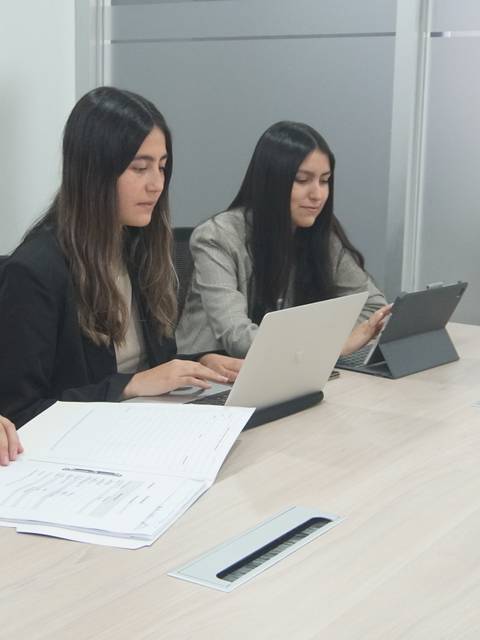 Tres mujeres trabajando en una clínica jurídica, utilizando computadoras y documentos en una mesa.