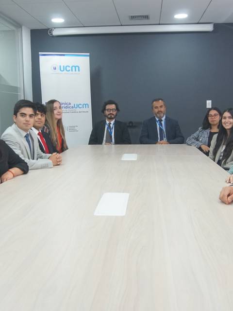 Un grupo de personas vestidas formalmente se sienta alrededor de una mesa en una sala de reuniones.