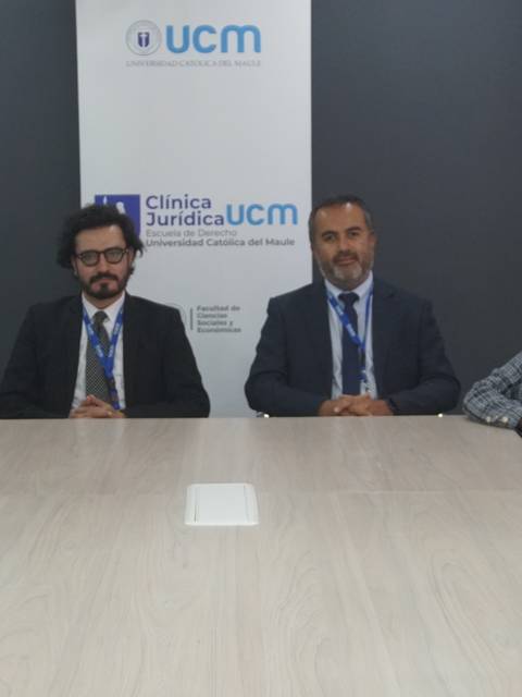 Un grupo de estudiantes y un profesor posan juntos en una sala de reuniones con un banner de la Clínica Jurídica UCM de fondo.