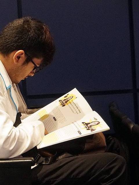Una persona está sentada en un auditorio leyendo un libro.