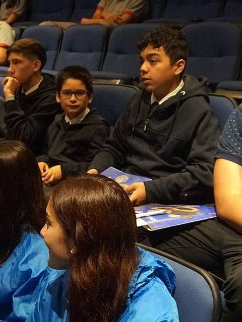 Un grupo de jóvenes sentados en un auditorio, algunos con ropa de abrigo y otros concentrados en la presentación.