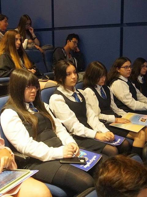 Un grupo de estudiantes sentados en un auditorio, atentos a una presentación.