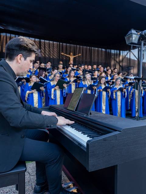 Un músico toca el piano mientras un coro actúa en un escenario al aire libre.