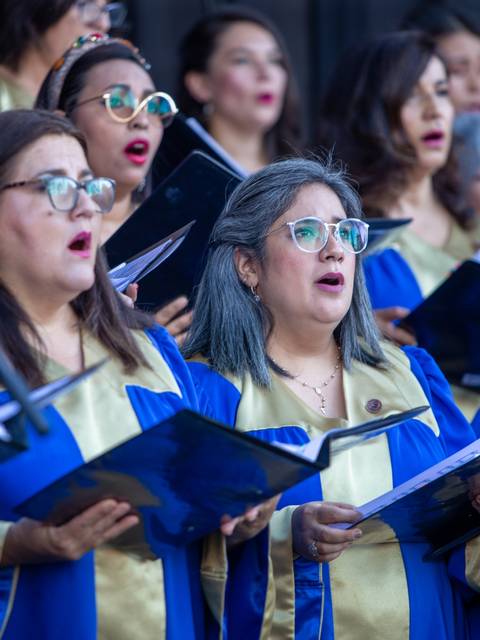 Un grupo de mujeres cantando en un coro, vestidas con túnicas azules y doradas.