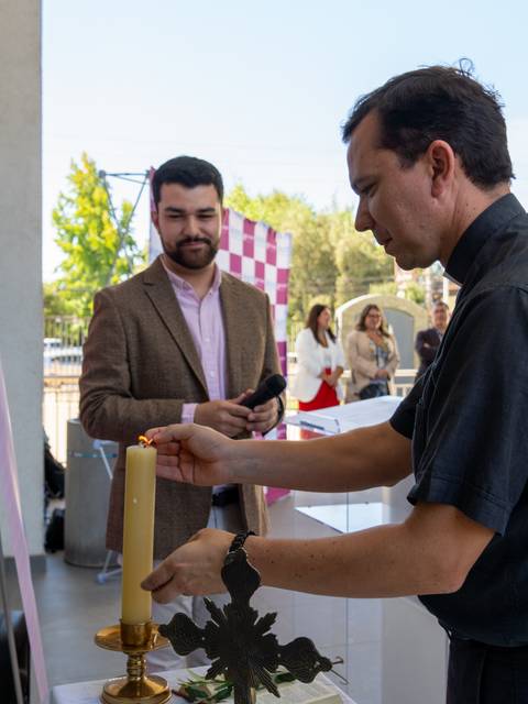 Un hombre vestido de negro enciende una vela en un evento al aire libre, mientras otro hombre lo observa.