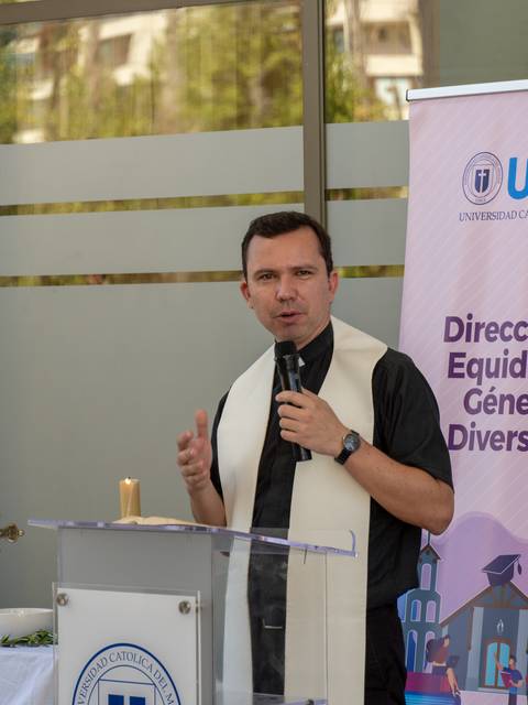 Un hombre está hablando en un evento, vestido con una camisa negra y una estola blanca, frente a un podio.