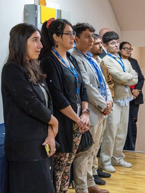 Un grupo de personas de pie en un evento, mirando hacia adelante.