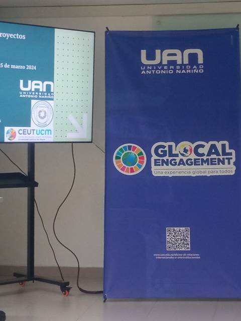 La imagen muestra a una mujer de pie junto a una pantalla que presenta un tema sobre pueblos indígenas y proyectos en Chile durante una presentación en una universidad.