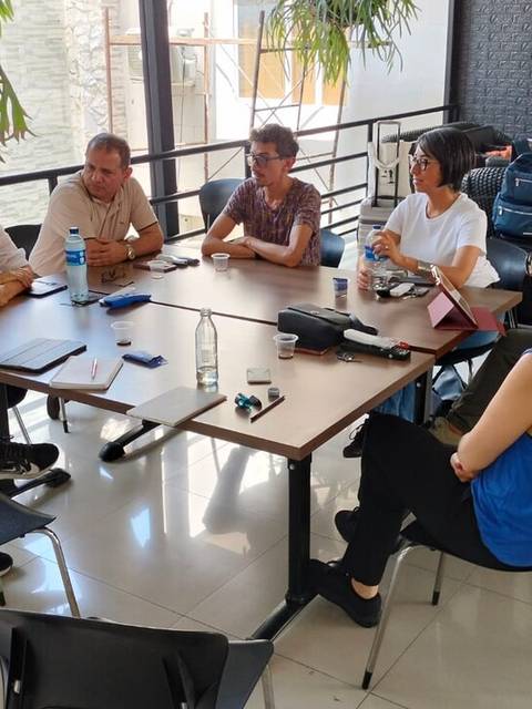 Un grupo de personas se reúne alrededor de una mesa para discutir en un ambiente informal.