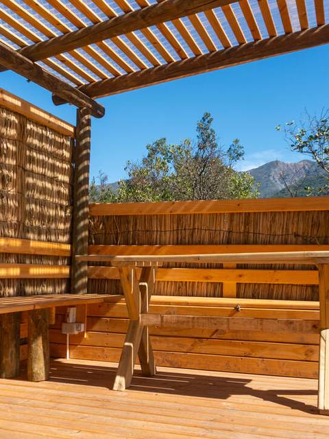 Un área de descanso al aire libre con muebles de madera, rodeada de vegetación y montañas.