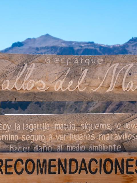 Un cartel de madera en un parque que ofrece recomendaciones sobre cuidados ambientales y seguridad en el camino.