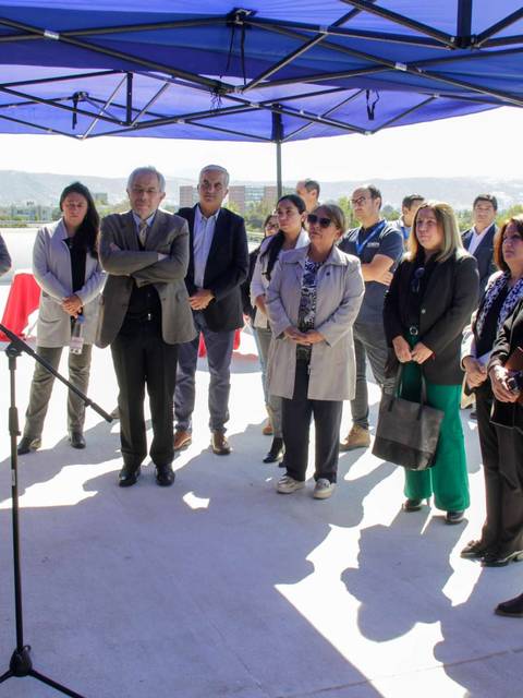Un grupo de personas escucha atentamente a un orador durante un evento al aire libre bajo una carpa.