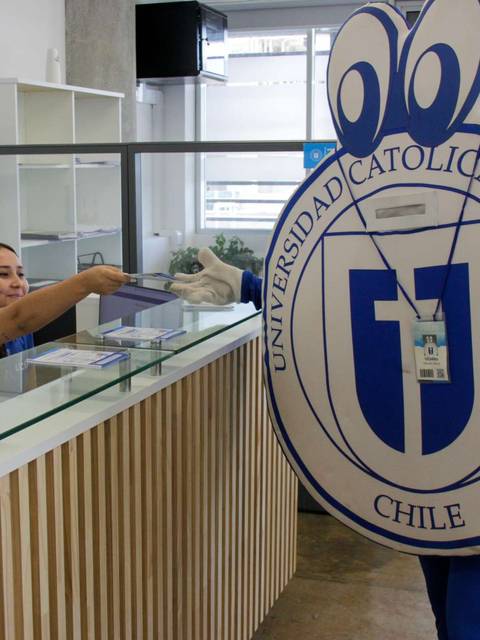 Una mujer en un mostrador entrega algo a un personaje disfrazado que representa a la Universidad Católica del Maule en Chile.