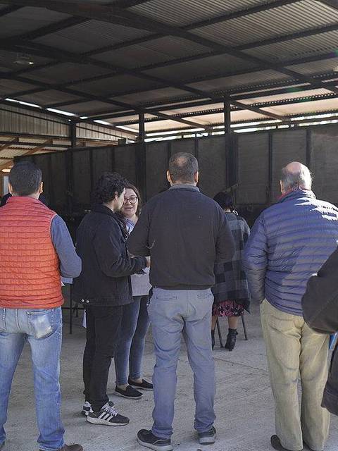 Un grupo de personas se encuentra reunido en un espacio al aire libre, frente a un cartel que promueve la producción comunitaria y el patrimonio cultural.
