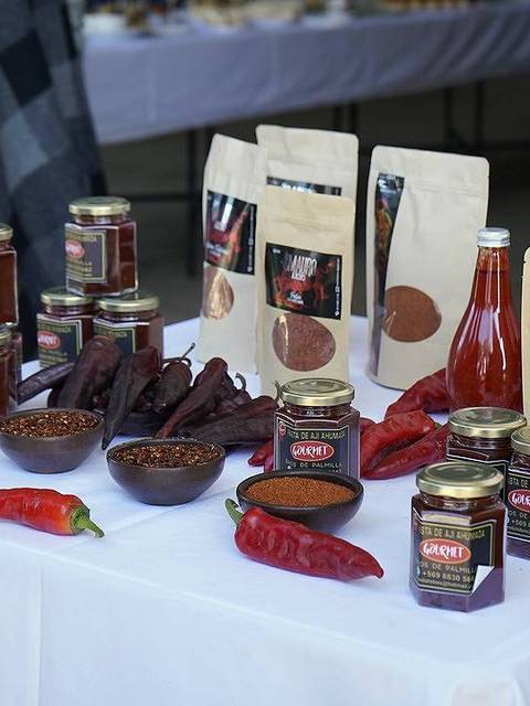 Mesa de mercado con una variedad de productos alimenticios en frascos y bolsas, incluyendo chiles y salsas.