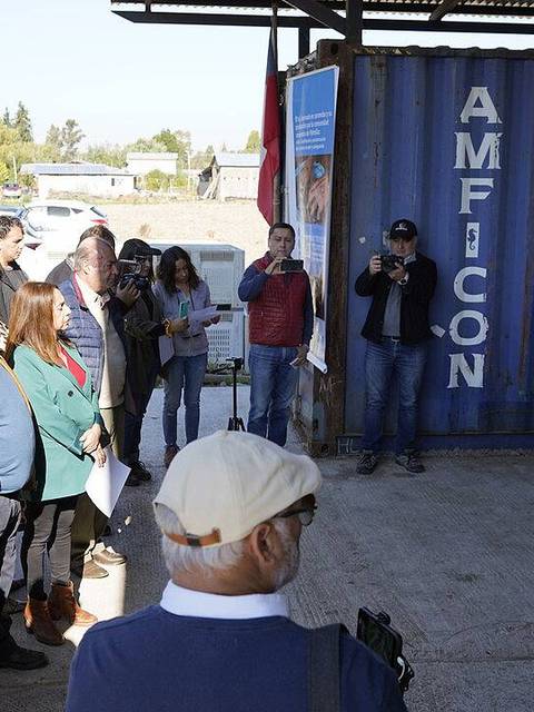 Un grupo de personas está reunido escuchando a un orador junto a un contenedor azul marcado con el nombre AMFICON.