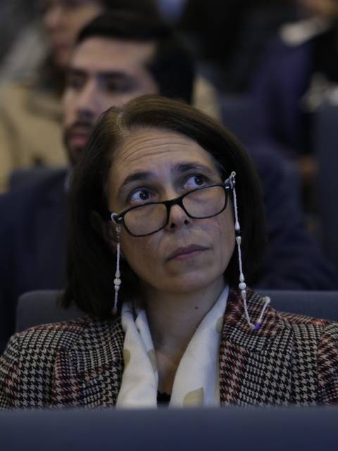 Una mujer con gafas observa atentamente una presentación en un auditorio.