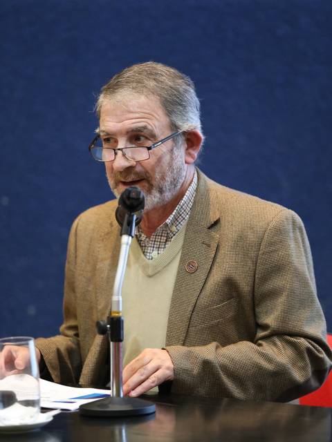 Un hombre habla en una mesa de conferencias frente a un micrófono.