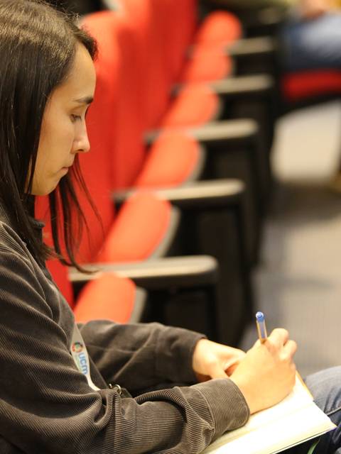 Una persona sentada en una sala escribe en un cuaderno.
