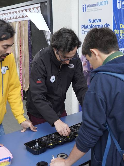 Un grupo de estudiantes interactúa en un evento frente a una mesa con objetos variados.