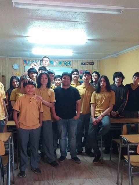 Grupo de estudiantes en un aula con paredes de madera y mesas de escuela.