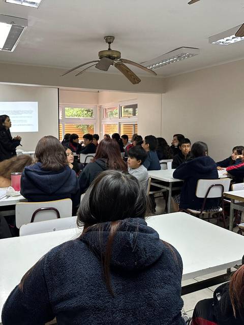 Un aula con estudiantes escuchando a una profesora que está dando una presentación.