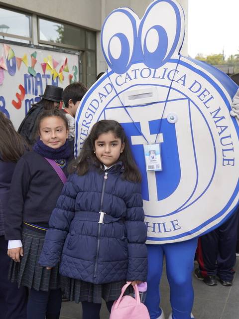 Un grupo de niñas posa junto a una mascota representativa de la Universidad Católica del Maule en un evento escolar.