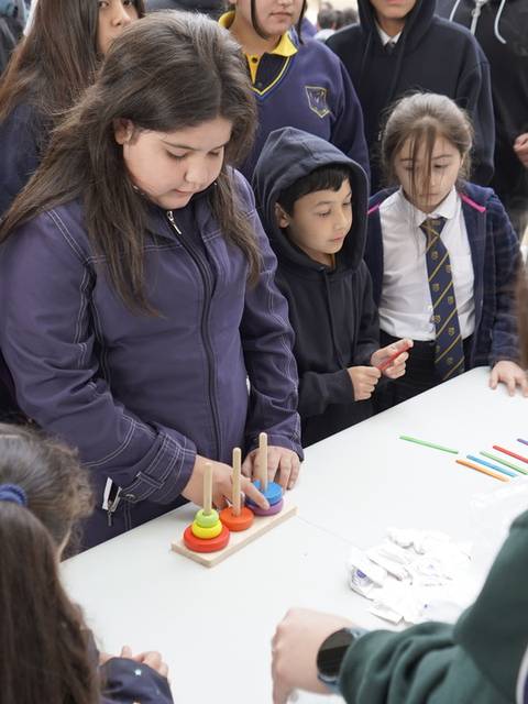 Un grupo de niños interactúa en una actividad al aire libre, concentrados en una mesa con objetos coloridos.