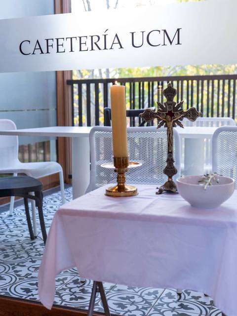 Una mesa en una cafetería con una vela encendida y una cruz decorativa en un ambiente moderno.