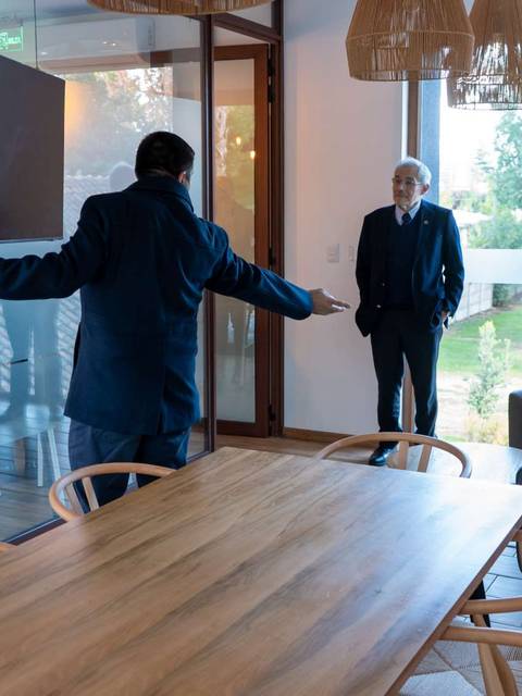 Un hombre presenta un espacio moderno mientras dos personas lo observan en una habitación amplia con un diseño contemporáneo.