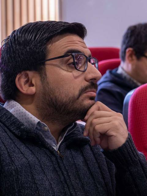 Un grupo de personas escuchando atentamente en una sala con asientos rojos.