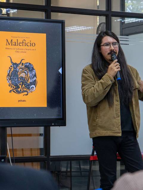 Un presentador habla sobre un libro titulado 'Maleficio' en un evento ante una audiencia.