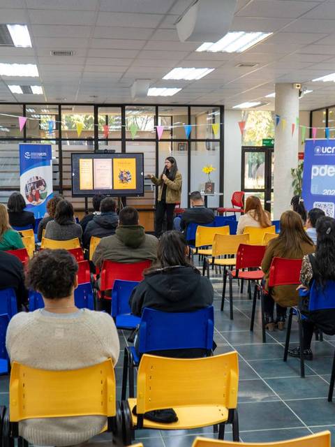 Una sala donde se lleva a cabo una presentación ante un grupo de personas sentadas en sillas de colores.