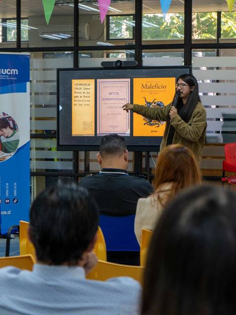 Una mujer presenta información en una pantalla mientras una audiencia observa atentamente.